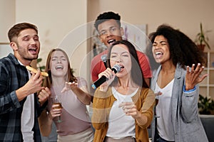 Awesome home party. Attractive young asian girl holding microphone and singing while playing karaoke with best friends