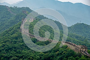 Awesome view of Great Wall of China with a green trees and rocky mountains in the background. Misty foggy air above the hills