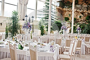 Awesome wedding hall with white chairs and purple flowers on tab