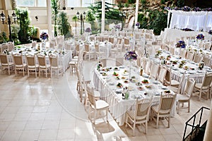 Awesome wedding hall with white chairs and purple flowers on tab