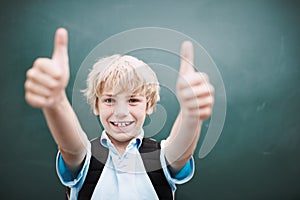 Awesome. A young schoolboy giving you a thumbs up while standing alongside copyspace at a blackboard.