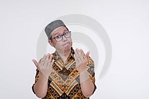 An awkward man challenges someone after being insulted by their comments. Wearing a batik shirt and songkok skull cap. Isolated on