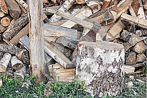 An ax in a wooden beam against the background of a pile of wooden firewood.