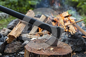 An Axe in a chopping block with a campfire behind