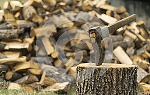 An axe stuck in a log in front of a pile of wood