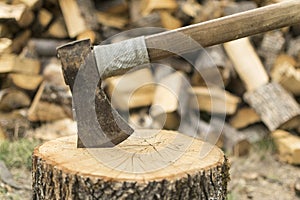 An axe stuck in a log in front of a pile of wood