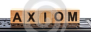 Axiom word made with building blocks. A row of wooden cubes with a word written in black font is located on a black keyboard