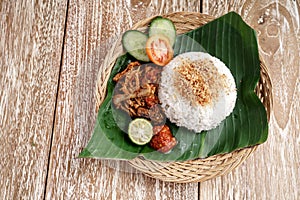 Ayam geprek with white rice and sliced of tomato, cucumber, lime and sambal