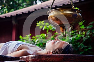 Ayurveda massage alternative healing therapy.beautiful caucasian female getting shirodhara treatment lying on a wooden photo