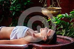 Ayurveda massage alternative healing therapy.beautiful caucasian female getting shirodhara treatment lying on a wooden photo