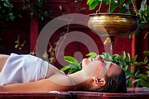 Ayurveda massage alternative healing therapy.beautiful caucasian female getting shirodhara treatment lying on a wooden photo