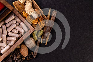 Ayurvedic drugs in a wooden box and assorted spices on black background. Herbs concept