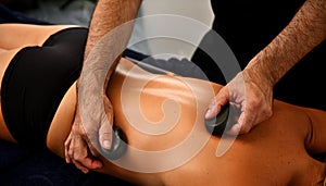 Ayurvedic hot stone massage in modern spa salon. Bodycare concept. Masseur massaging woman`s back with lava stones