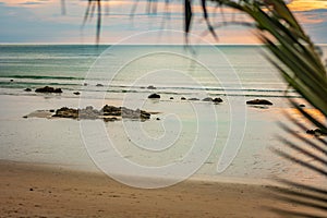 The azure coast, the beach on the island of Thailand, the sunset, the rocks by the shore and the blurred palm tree