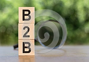 B2B Word On Wooden Blocks on table with magnifier on green background