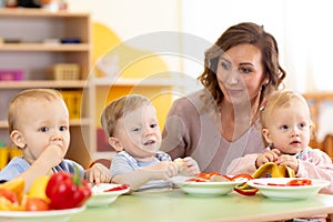 Babies and carer together eat fruits and vegetables as a snack in the kindergarten, nursery or daycare