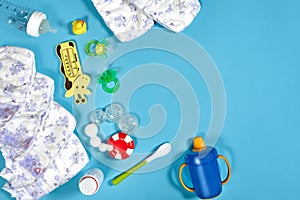 Babies goods: cloth diaper, baby powder, nibbler, cream, teether, soother, baby toy on blue background. Copy space. Top photo