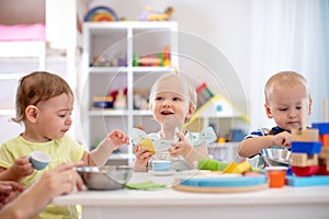 Babies playing together in the kindergarten or creche. Kids sitting at table in nursery or daycare