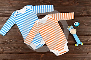 Babies striped bodysuits, toy and pacifier on wooden background. photo