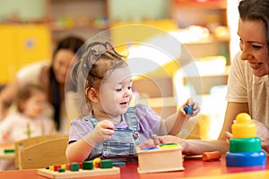 Babies with teachers play with developmental toys in nursery