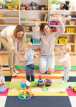 Babies toddlers playing with colorful educational toys together with mothers in nursery room