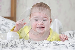 Baby 6-7 months crying lying on his stomach. A caucasian baby in yellow is crying and showing 2 baby teeth, teething