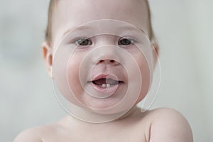 Baby 6-7 months smiling showing first teeth, baby face close-up portrait. Pretty baby girl boy puffy cheeks