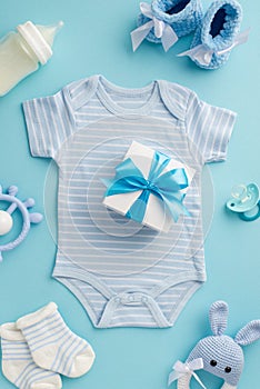 Baby accessories concept. Top view vertical photo of giftbox over bodysuit socks baby`s dummy teether milk bottle booties and