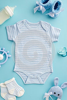 Baby accessories concept. Top view vertical photo of infant clothes bodysuit booties socks baby`s dummy teether milk bottle and