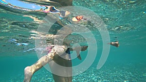 The baby actively moves his legs under water. One year old boy swims in the sea, the mother holds the child