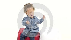 Baby of an african american is sitting on a pillow and is dancing. White background. Slow motion