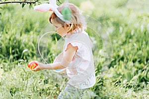 Baby with basket full of colorful eggs. Easter egg hunt.