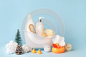 Baby bath cosmetics in toy bathtub with christmas decorations on blue bakground, copy space