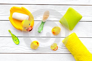 Baby bath set with yellow rubber duck. Soap, sponge, brushes, towel on white wooden background top view