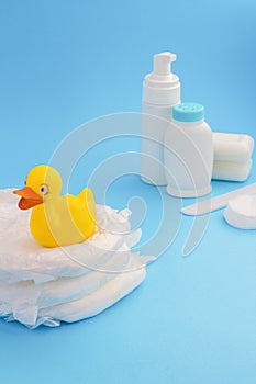 Baby bath time. Cute yellow duckling sitting on diapers pile. Cream, lotion and soap. Powder, cotton wool and comb