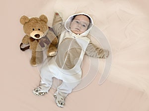 Baby and bear. A beautiful smiling toddler lies on the bed next to his favorite soft toy.