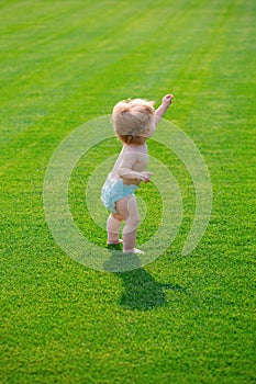 Baby in beautiful spring green field. Warm spring time in the park in diaper pants.