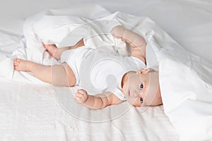 Baby on the bed in the morning. Textiles and bed linen for children. A newborn baby has woken up or is going to bed