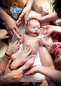 Baby with big eyes being touched by relatives' hands photo