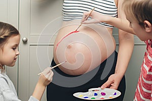 Baby birth expecting time and belly painting. Happy children and pregnant mom having fun together at home