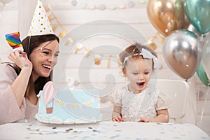 Baby birthday party. Mother and her daughter celebrate and fun together. Child party with balloons decoration and cake