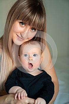 Baby in black clothes yawns in the arms of mother.