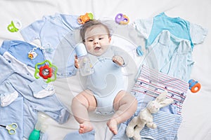 A baby in blue clothes is lying among children`s accessories and clothes