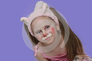 baby with blue eyes and baby makeup. A child with a funny face pattern. Bunny makeup on a child's face. Purple background