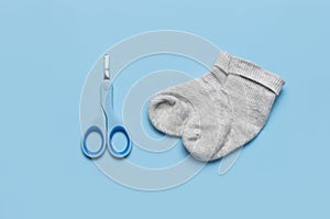 Baby blue scissors for hygiene and baby socks on blue background top view flat lay copy space. Metal and plastic baby nail