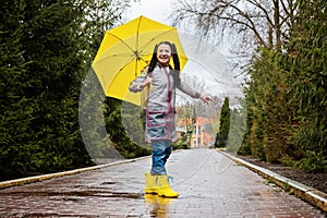 Baby Boomers Happy senior woman in yellow rain coat with yellow umbrella jumping and enjoying life in park.