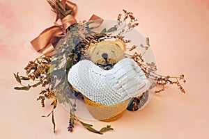 Knitted baby bootee, toy bear and bouquet of flowers on soft pink background. Birth of a child concept.