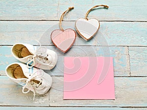 Baby booties and two hearts on the wooden background, close up.