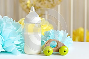 Baby bottle with breast milk, various festive paper decor in front of baby bed. It`s a boy or baby birthday celebration concept.