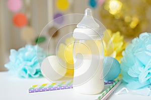Baby bottle with breast milk, various festive paper decor in front of baby bed. It`s a boy or baby birthday celebration concept.